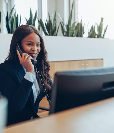 Two smiling businesswomen talking on telephones at an office reception